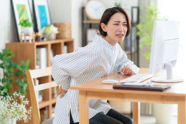 デスクワーク中に腰の痛みを訴える女性